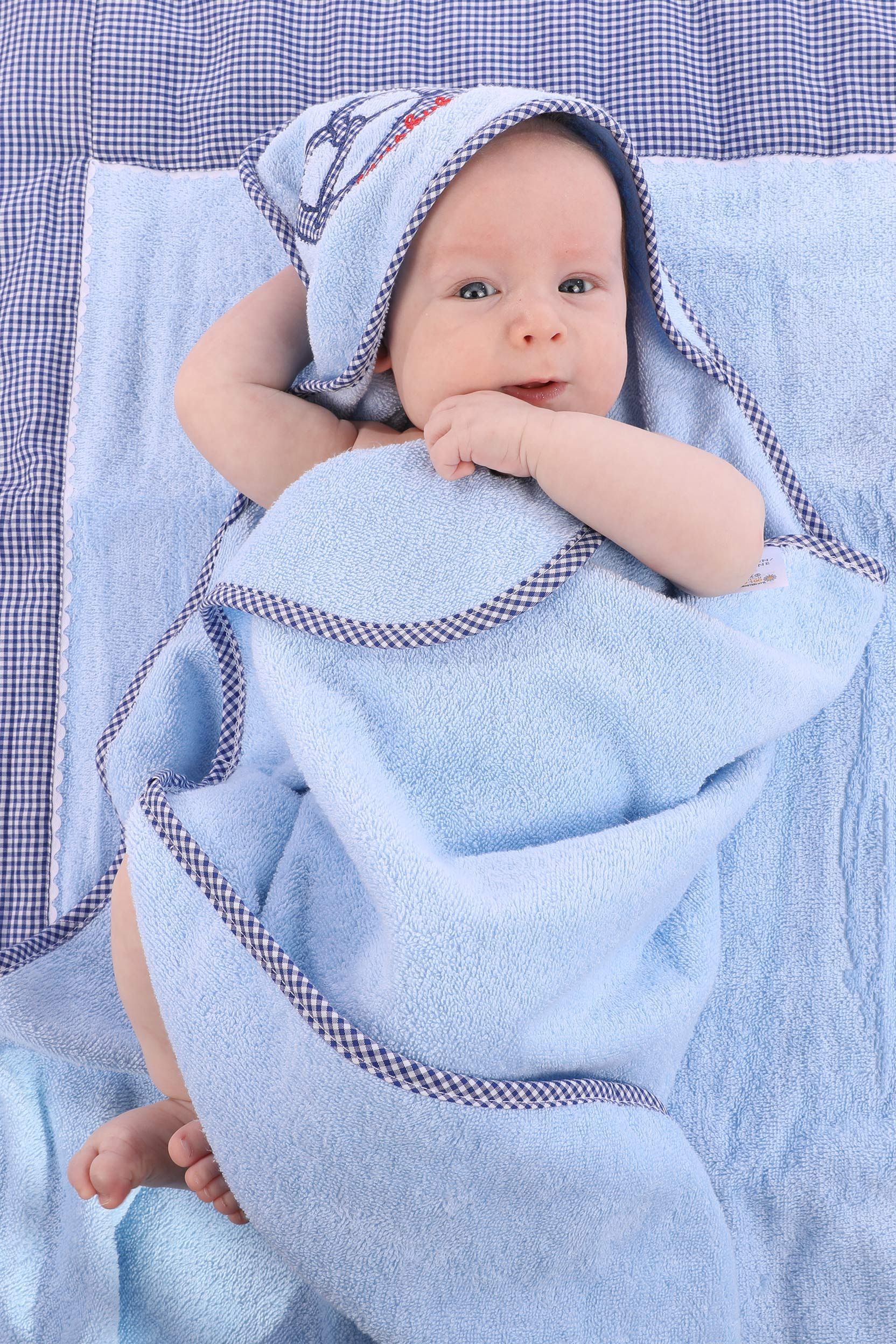 Ein Baby in einem blauen Handtuch mit karierter Einfassung liegt auf einer Decke.